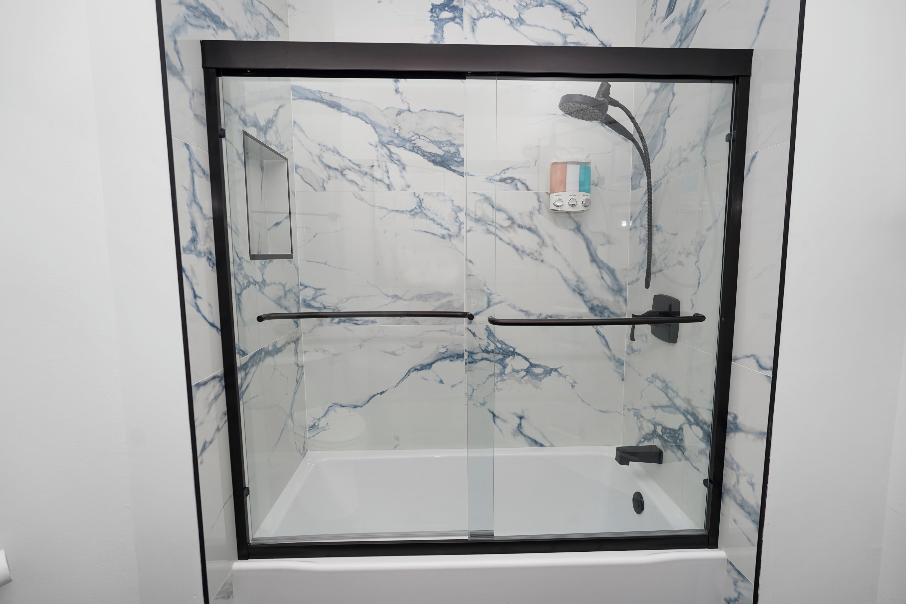 Ducha con cerramiento de vidrio, pared de mármol, panel de control y cabezal de ducha manual.
