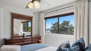 Quarto com uma cama grande, penteadeira, espelho e janela com vista para árvores e uma torre.