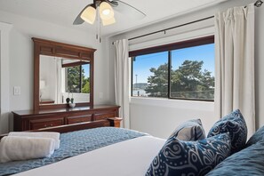 Ein Schlafzimmer mit einem großen Bett, einem Schminktisch, einem Spiegel und einem Fenster mit Blick auf Bäume und einen Turm.