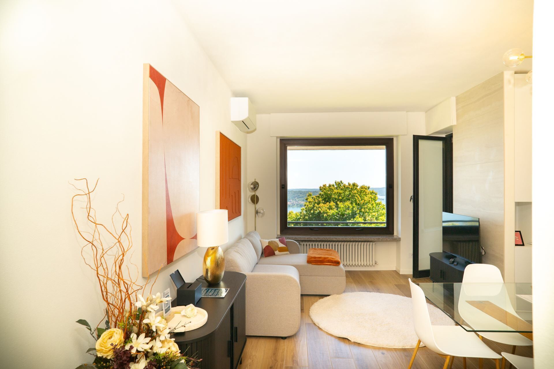 A modern living room with a sofa, a glass table, and a view of greenery through a large window.