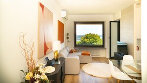 Ein modernes Wohnzimmer mit einer Couch, einem Glastisch und Blick auf Grün durch ein großes Fenster.