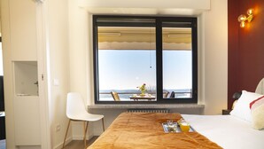 Ein Hotelzimmer mit großem Fenster, einem Bett mit brauner Decke, einem weißen Stuhl und einem Tisch mit Frühstücksgebäck.