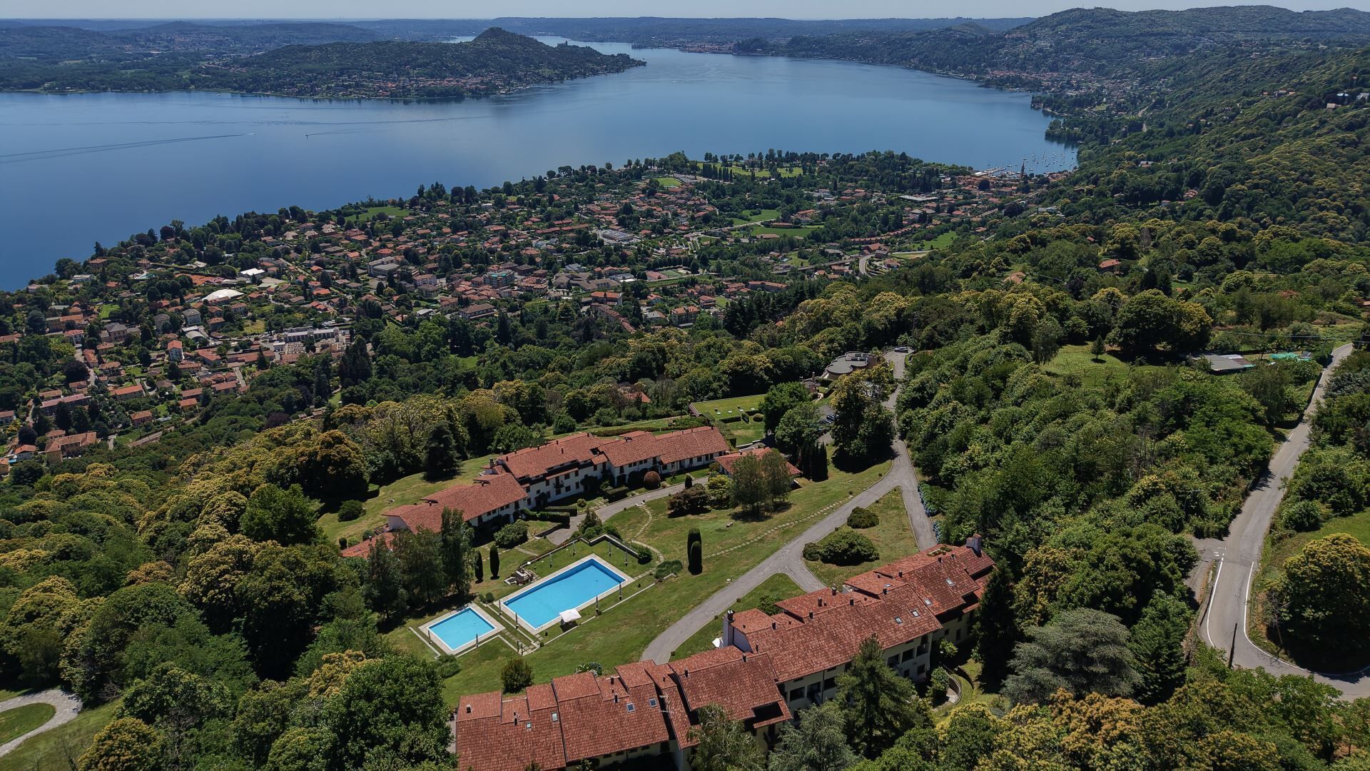 An aerial view of a residential area with a large lake, surrounded by greenery and houses with red-tiled roofs.