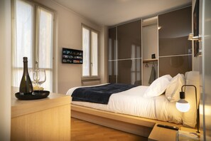 A bedroom with a bed, bedside table, lamp, and a TV screen. - Corte Cavour in the City Center (Gallarate)