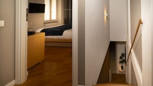 Ein Flur, der in ein Schlafzimmer mit Bett, Kommode und Fenster führt.