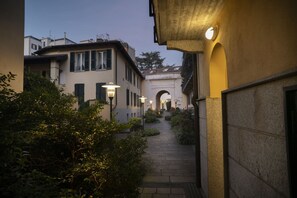Une ruelle étroite bordée de bâtiments des deux côtés, un sentier pavé et un arc de triomphe visible au loin.