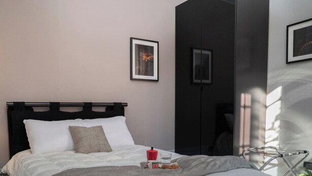 A hotel room with a bed, bedside table with a lamp, a small table with a cup and a glass, and a wall-mounted picture. - Bianca in the Heart of the City (Somma Lombardo)