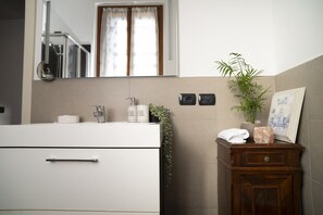 A bathroom with a white vanity, a mirror, a sink, a faucet, a potted plant, a towel, a salt block, and a picture frame. - Bianca in the Heart of the City (Somma Lombardo)
