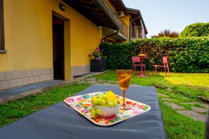A table with a fruit bowl and a glass, set on a mat outside a yellow building with a door and a window. - Da Gise: Garden, Wifi, Malpensa (Somma Lombardo)