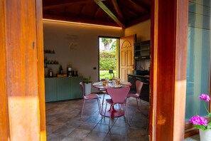 A dining area with a round table, pink chairs, and a view of a kitchen and outdoor greenery. - Da Gise: Garden, Wifi, Malpensa (Somma Lombardo)