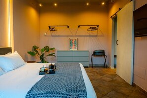 Een hotelkamer met een bed, nachtkastje, een plant, een wanddecoratie en een stoel.