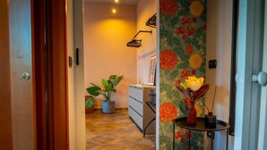 Ein Korridor mit einer Holztür, einem Blumentopf, einem kleinen Tisch mit einer Vase und einer Wand mit floralem Wandpapier.