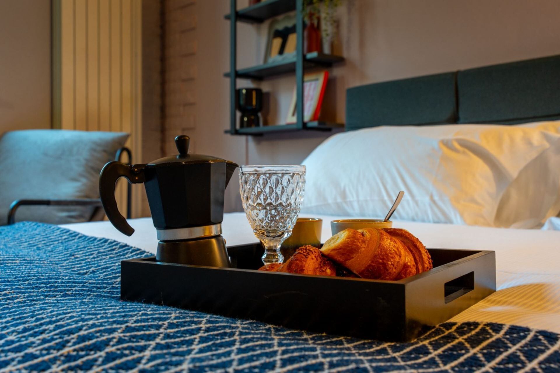 Un vassoio con una caffettiera, un bicchiere e croissant su un letto.