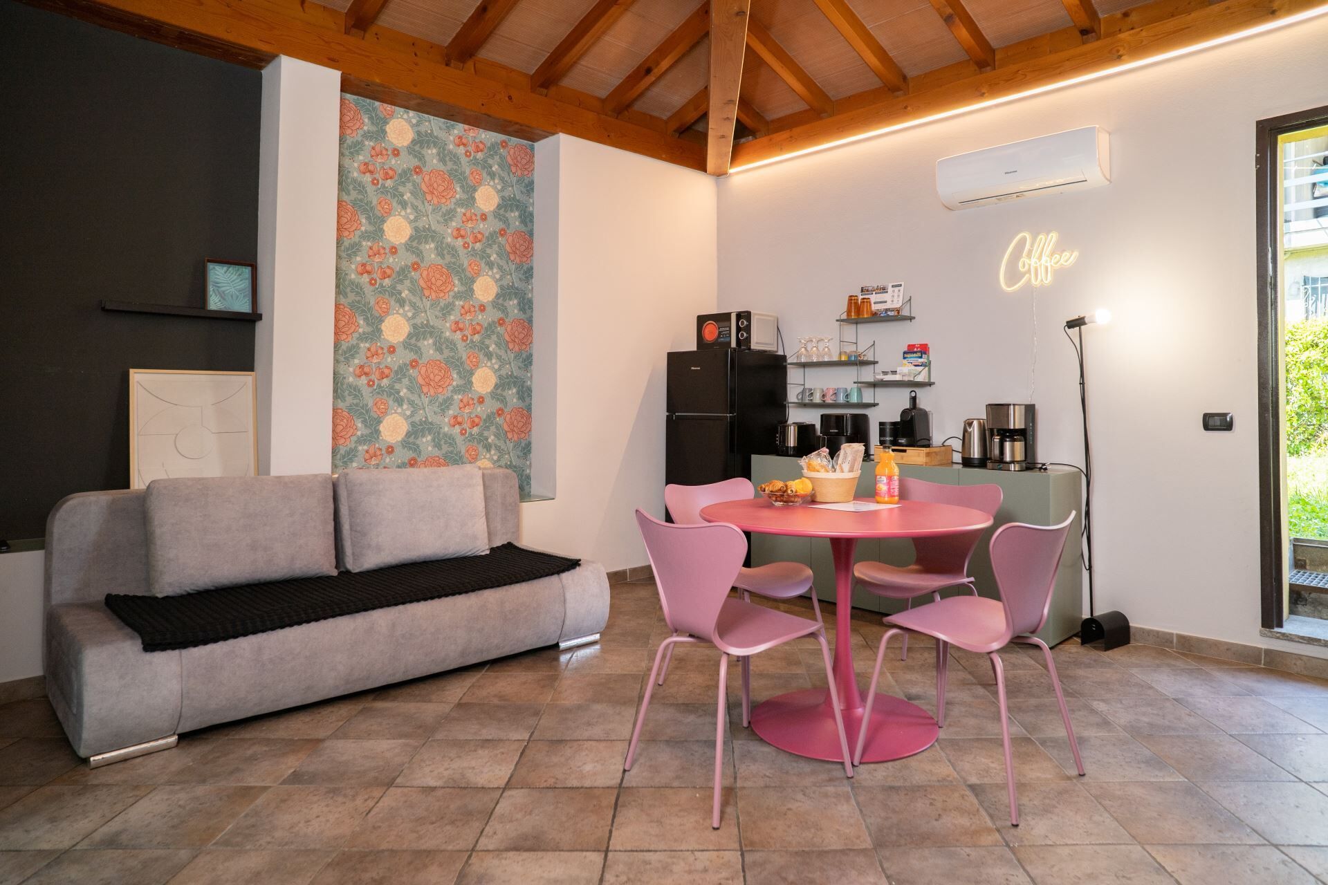 Una sala acogedora con sofá, una mesa redonda con sillas, una cocina equipada y una pared con estampado floral.
