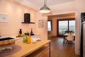 A modern kitchen with a wooden countertop, a hanging light fixture, and a view of a dining area with a table set for two. - Da Gregorio: The Lake View Belvedere with Pools (Gignese)