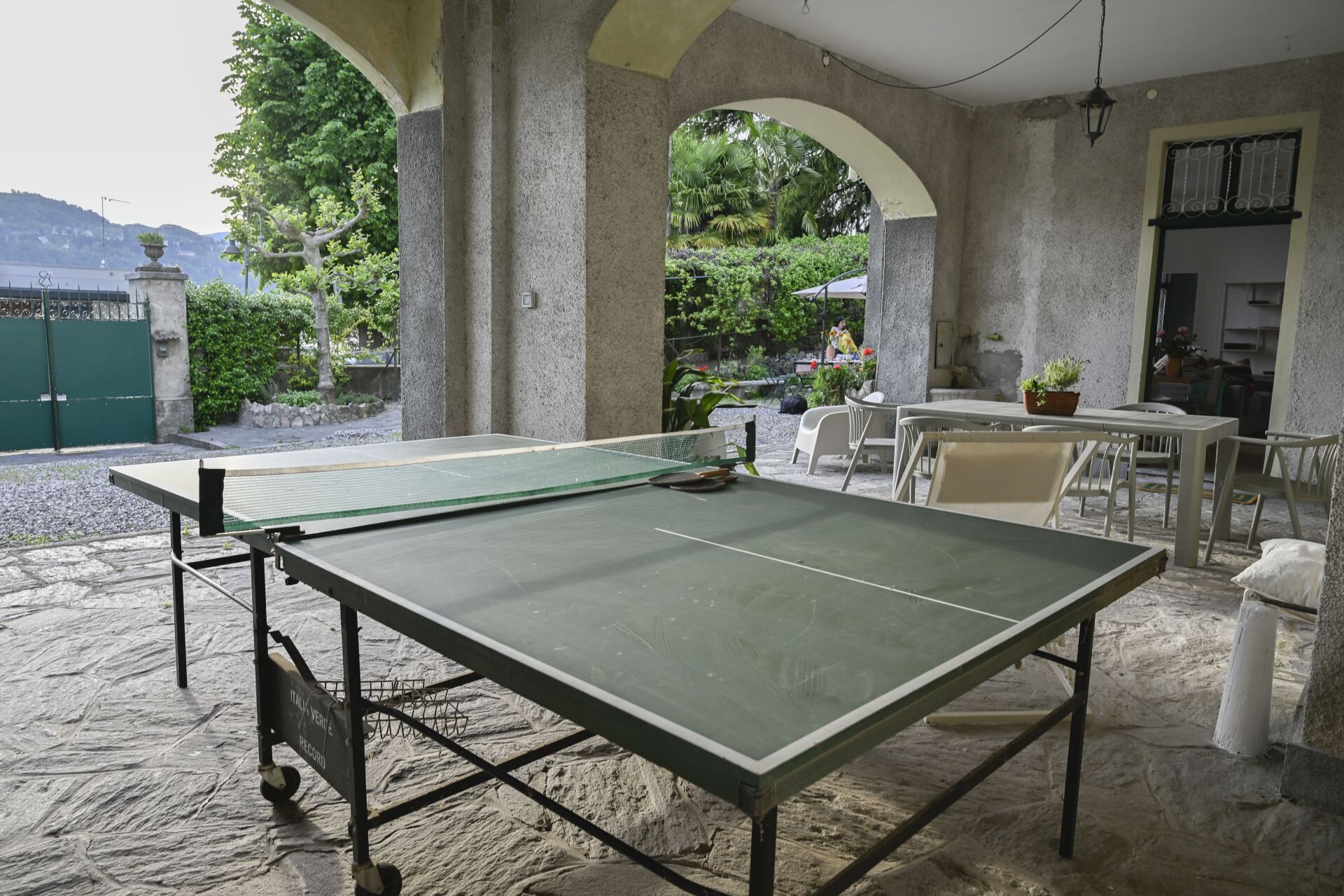 Une table de ping-pong installée dans un espace extérieur doté d’un sol en pierre, de chaises blanches et offrant une vue sur la verdure et les montagnes.