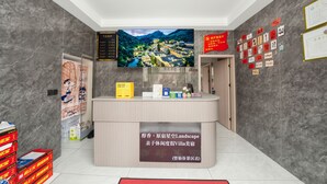 Un mostrador de recepción con un amplio cartel de paisaje, una pantalla digital y una pared con varios avisos.