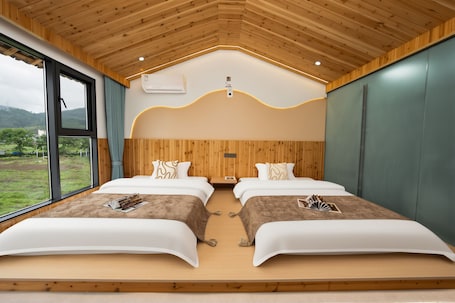 A room with two beds, wooden ceiling, large windows, and a view of greenery.. Wangxian Valley Scenic Area Chunxiang