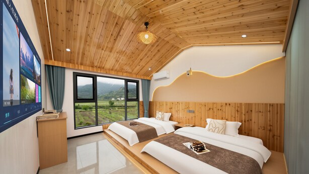 Un dormitorio con dos camas, techo de madera, un ventanal con vistas y televisor montado en la pared.