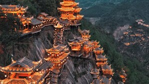 Un complejo de pagodas tradicionales de varios niveles, con techos escalonados e iluminado por una luz cálida, con montañas al fondo.