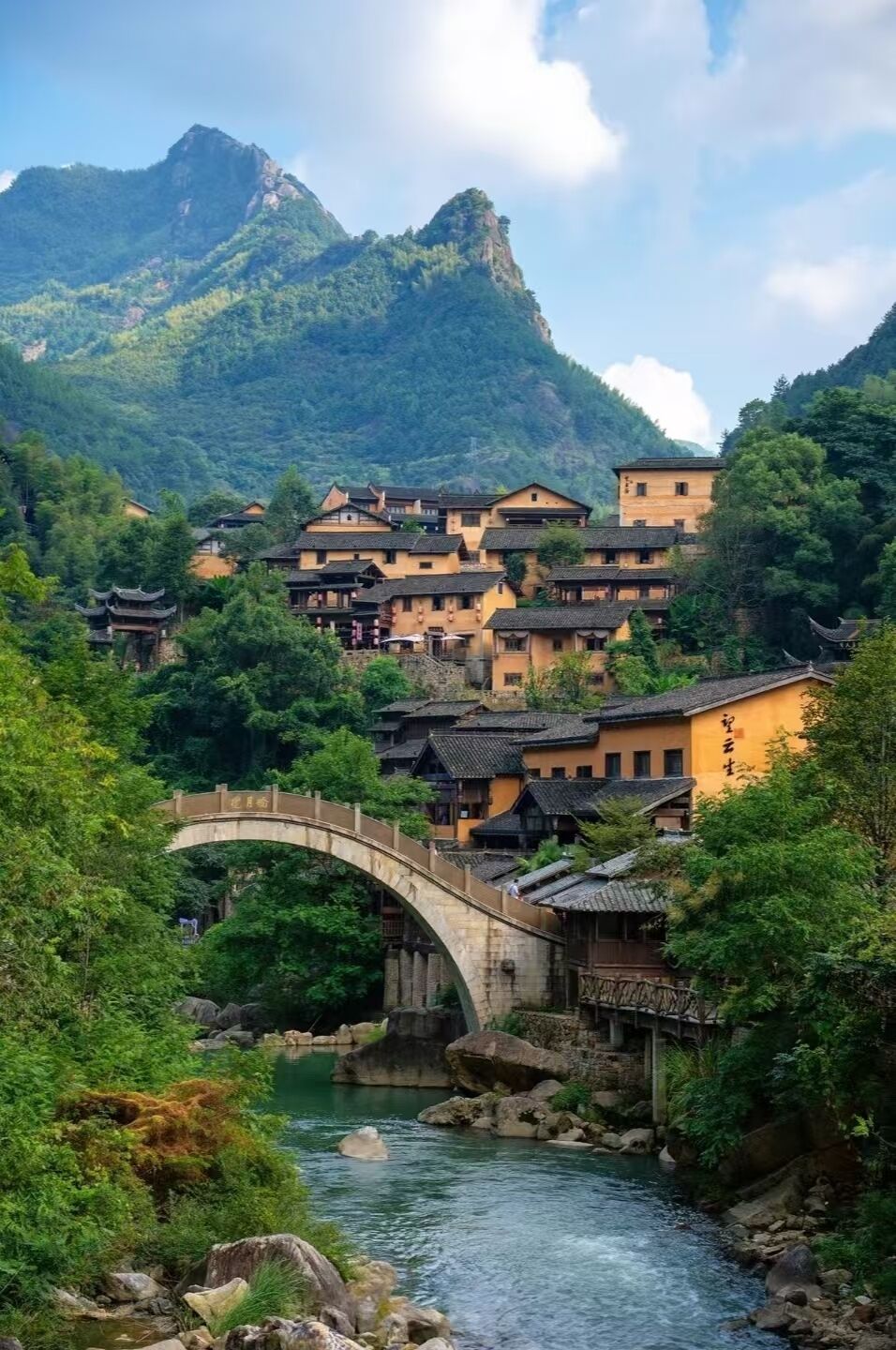 Un village traditionnel avec des bâtiments en pierre, un pont de pierre et une rivière.