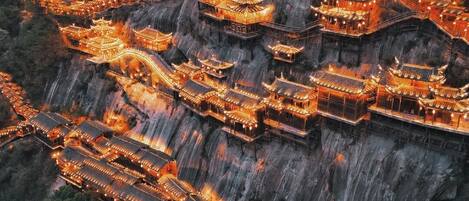 A traditional multi-tiered pagoda-style building complex with multiple levels and a central tower, surrounded by steep cliffs and dense forest.