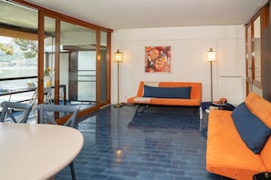 A room with a glass door leading to a balcony, a sofa, a table, and a floor lamp. - Henriette Apt Terrace, Lake Access (Angera)