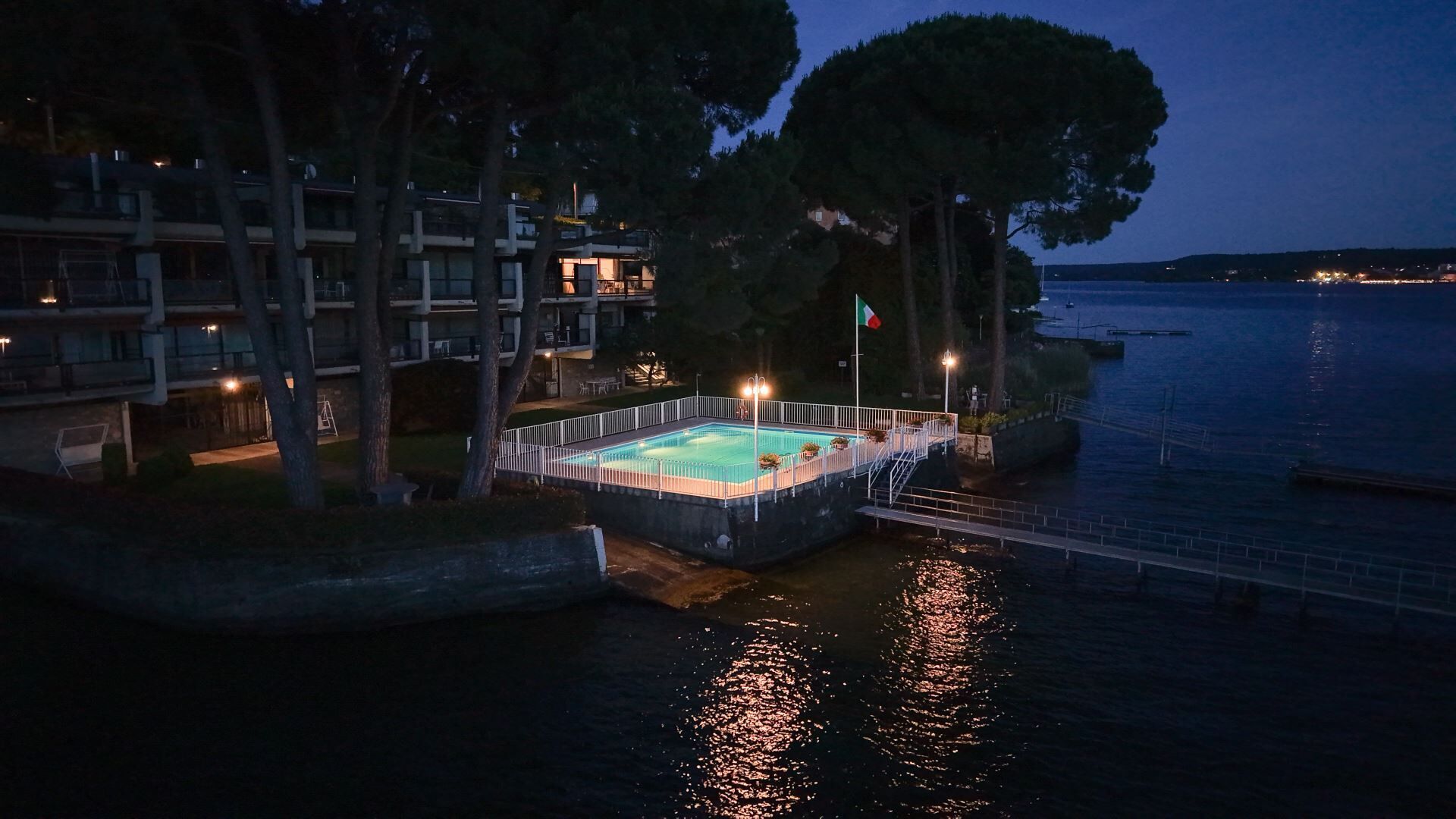 Una piscina envoltada per una tanca blanca, amb un vèrtex i un moll que s'estén a l'aigua.