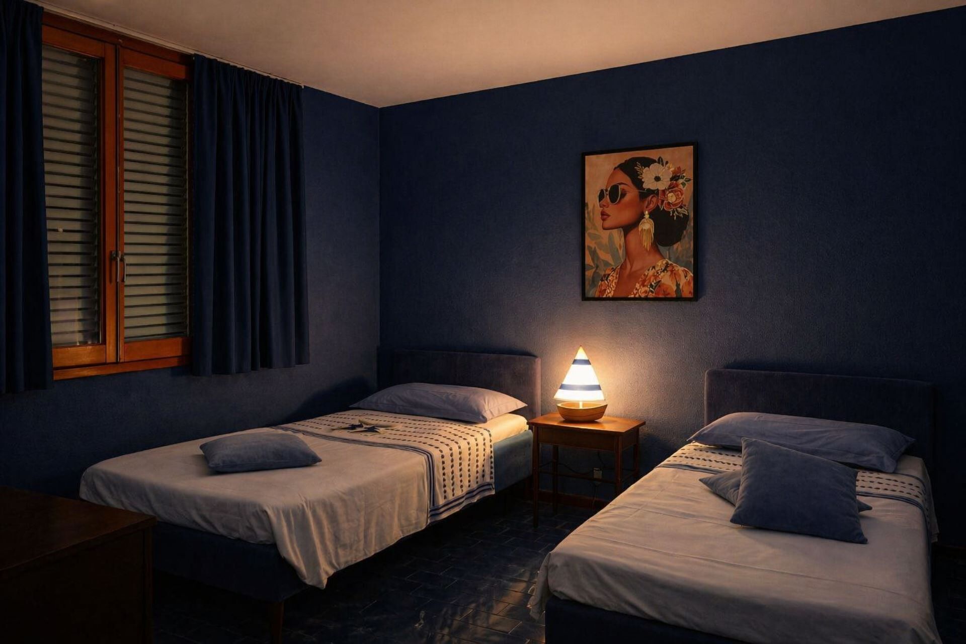 Ein Zimmer mit zwei Betten, einem Nachttisch mit Lampe, einem Bild an der Wand und einem Fenster mit Vorhängen.