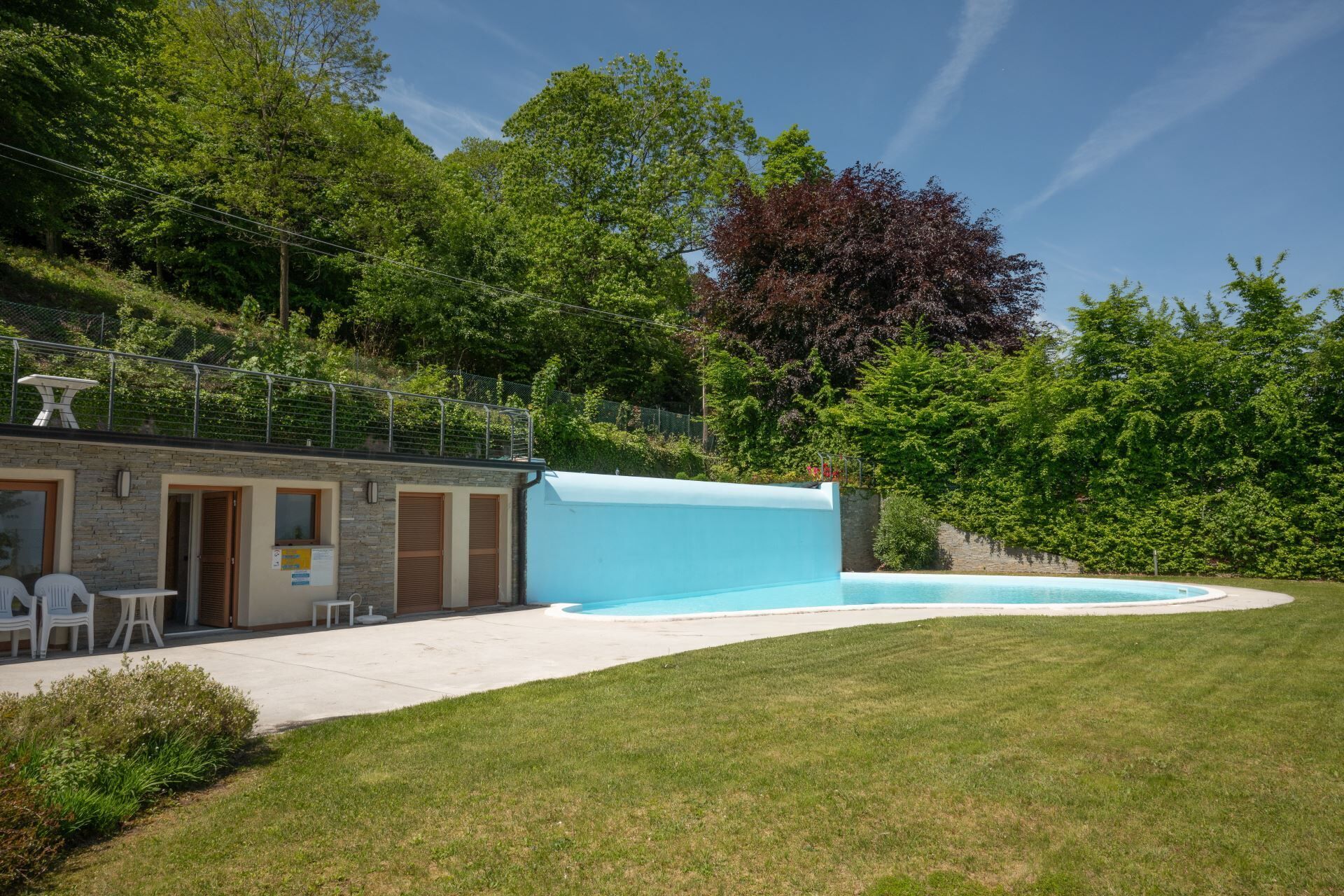 Un edificio moderno con piscina, area salotto esterna e uno sfondo collinare.