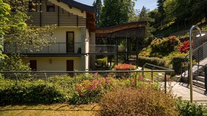 A modern building with a balcony, a staircase, and a garden with various plants and flowers. - LAKESCAPE apartment with terrace, view and pools (Gignese)