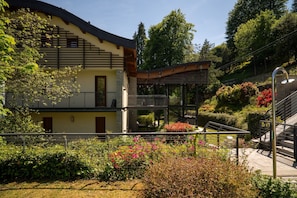 Ein modernes Gebäude mit Balkon, Treppe und einem Garten mit verschiedenen Pflanzen und Blumen.