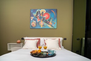 A hotel room with a bed, pillows, a painting on the wall, and breakfast items on the bed.