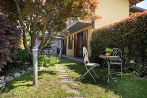 A garden with a pathway, a metal chair, a small table, and a building with a yellow facade.