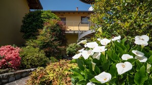 Ein Innenhof mit einem gelben Gebäude, einem Pflasterweg und verschiedenen grünen Sträuchern und Blumen.