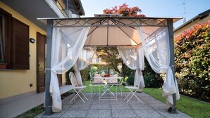 Eine überdachte Terrasse im Freien mit Tisch und Stühlen, umgeben von einem Garten.