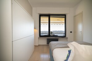 A bedroom with a bed, a window with a view, a radiator, and a door. - Blue Horizon - pools, terrace and lakes view (Lesa)