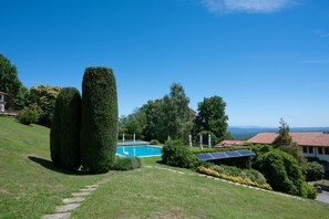 A landscaped garden with a swimming pool, neatly trimmed hedges, and solar panels. - Blue Horizon - pools, terrace and lakes view (Lesa)