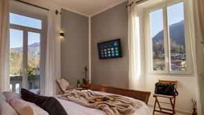Een slaapkamer met een bed, een televisie, een raam met uitzicht op bergen en een stoel.