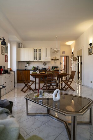 Eine moderne Küche mit weißen Schränken, ein Essbereich mit einem Glastisch und ein Wohnzimmer mit einer Couch und einem Couchtisch.
