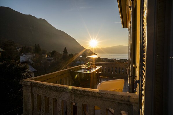 Ein Balkon mit Essplatz, der auf eine Berglandschaft und ein Gewässer im Sonnenuntergang blickt.