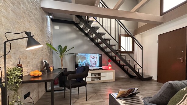 Uma sala de estar moderna com escada, televisão, escrivaninha com um laptop e sofá com revistas.
