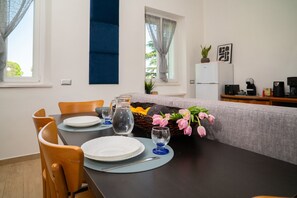 Ein Essbereich mit einem Tisch für vier Personen, einer Couch, einem Kühlschrank und einer Kaffeemaschine.