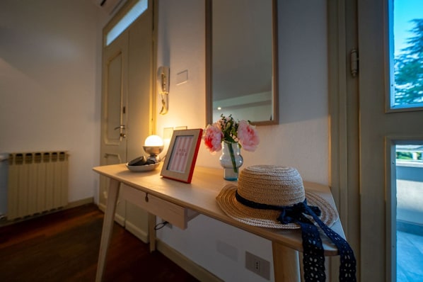 A room with a wooden desk, a framed picture, a vase with flowers, a hat, and a radiator.