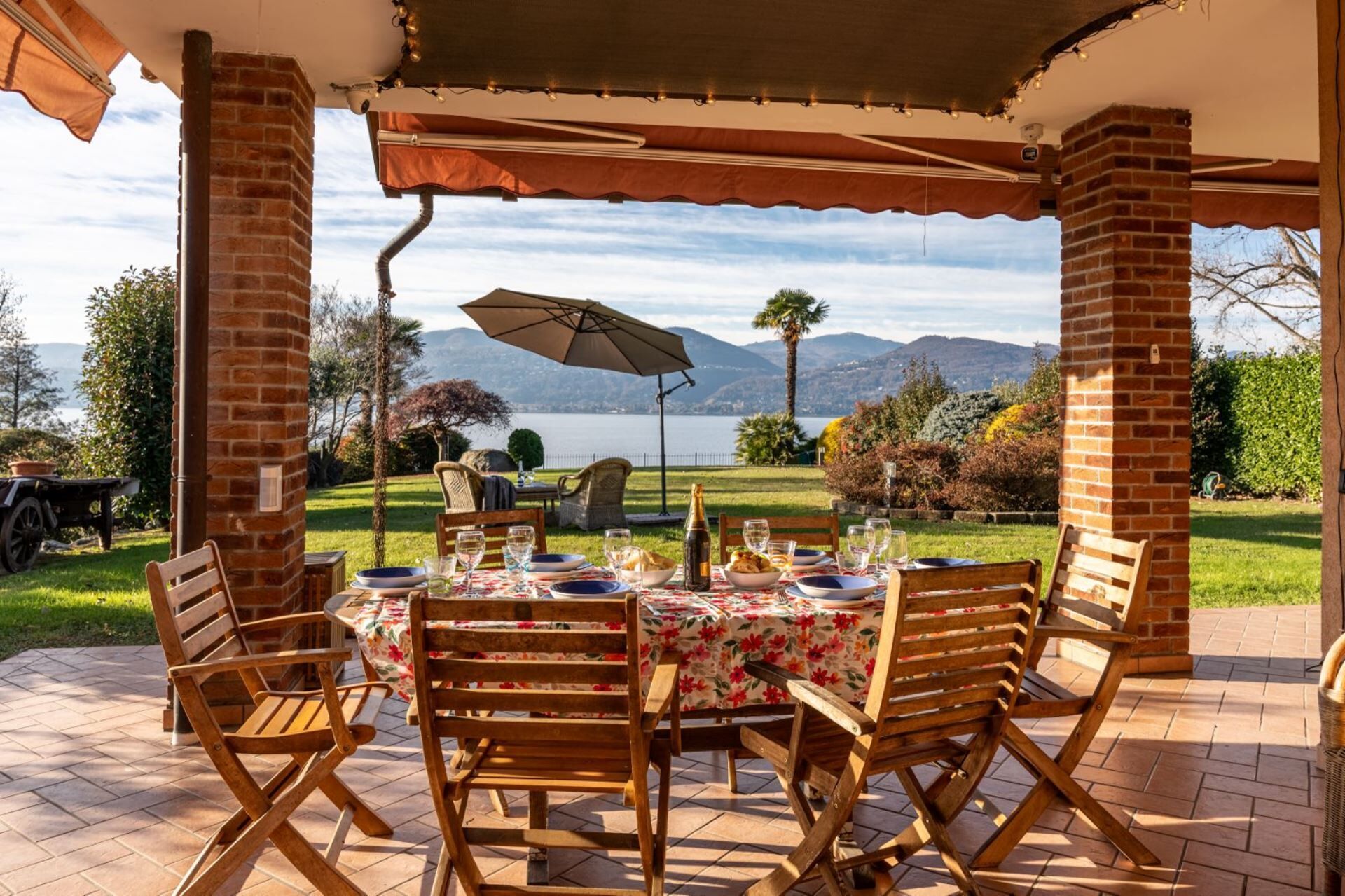 Une terrasse extérieure avec une table dressée pour le repas, entourée de piliers en briques, et offrant une vue panoramique sur un paysage magnifique avec des montagnes et une étendue d’eau.