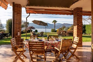 Eine Terrasse im Freien mit Esstisch, umgeben von Ziegelpfeilern, mit Blick auf eine malerische Landschaft mit Bergen und einem Gewässer.