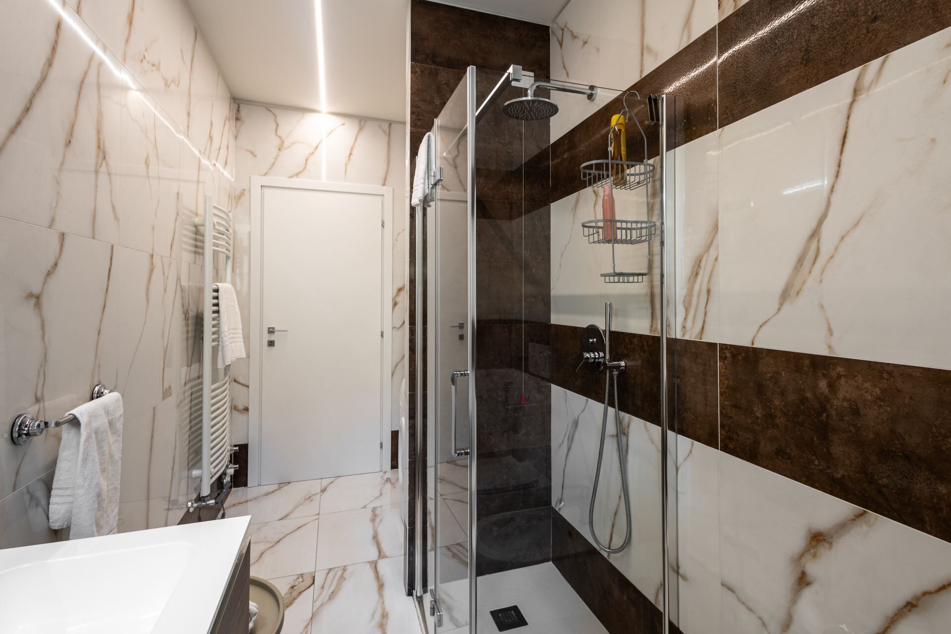 Une salle de bain moderne avec une douche à parois de verre, des murs en marbre et un lavabo blanc.