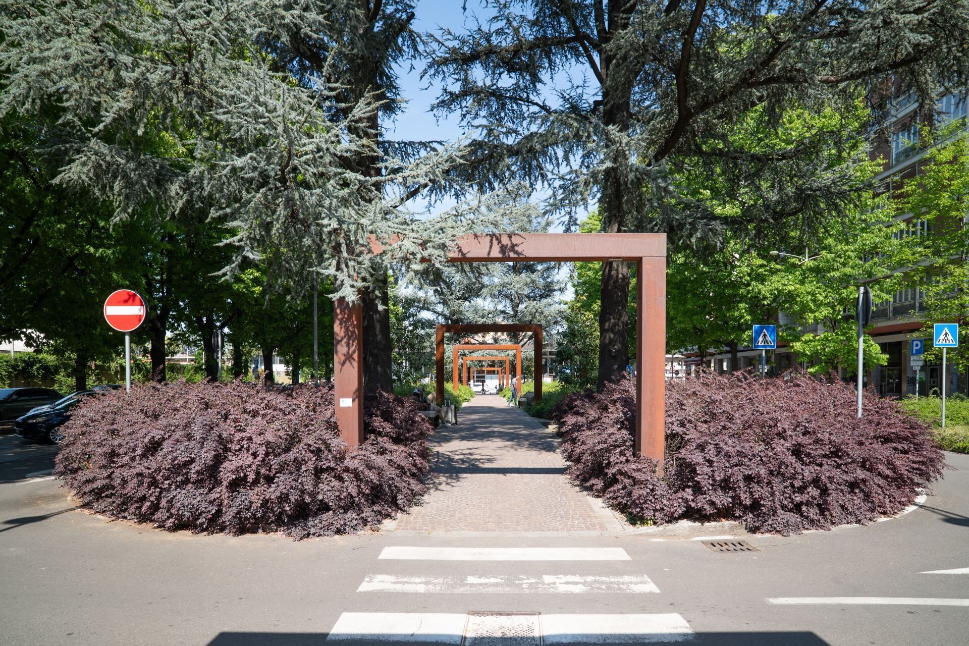 Un chemin piétonnier menant à l’entrée d’un bâtiment, bordé d’arbres et d’arbustes.