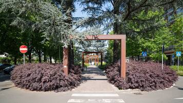 Un chemin piétonnier menant à l’entrée d’un bâtiment, bordé d’arbres et d’arbustes.