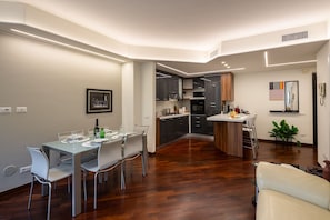 Een moderne keuken met donkere kasten, een centraal eiland en een eethoek met een glazen tafel en witte stoelen.